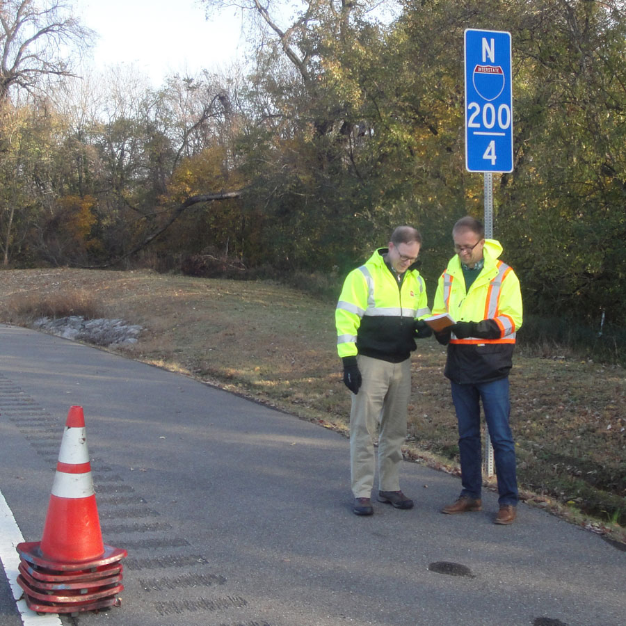 A picture of two men alongside the interstate, taking notes.