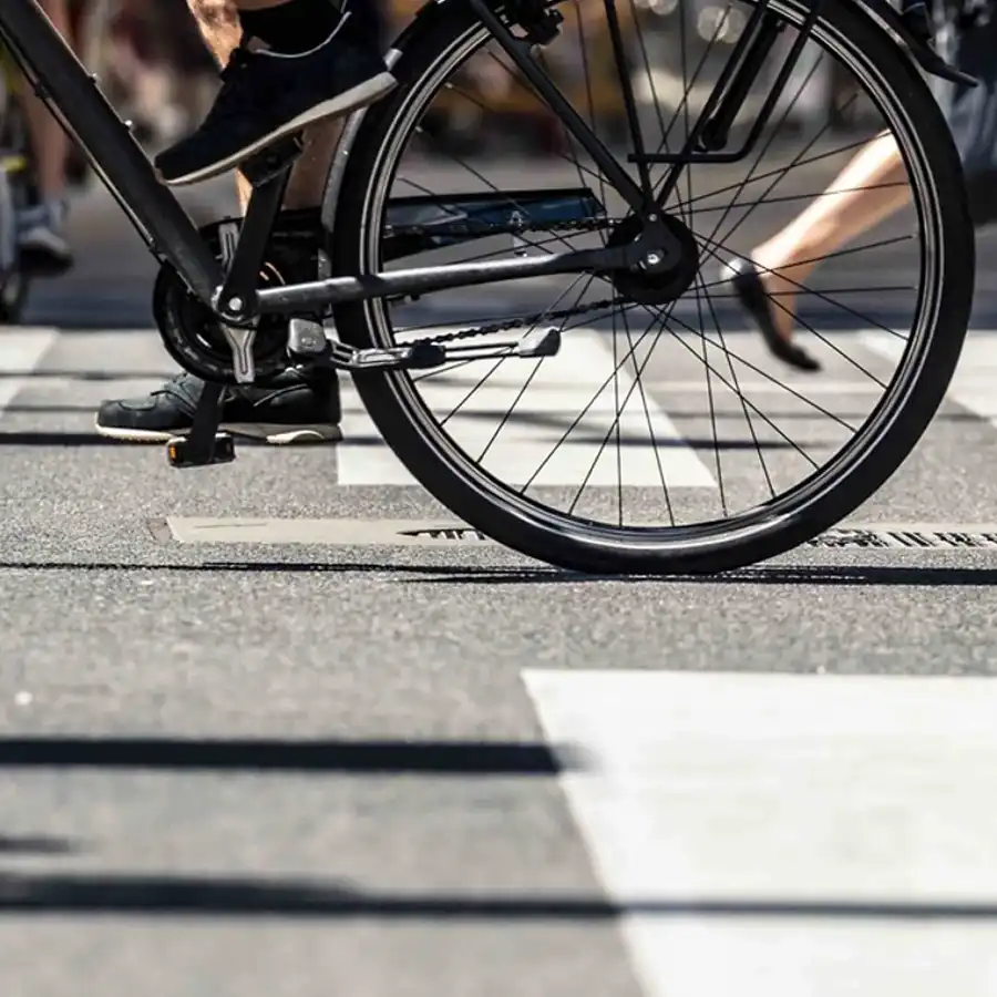 A photo of a bike wheel and feet on a crosswalk.