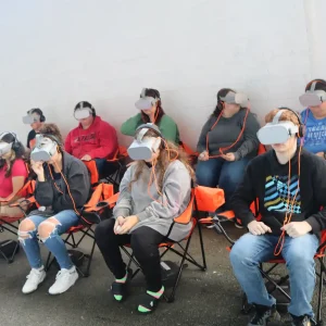 A photo of students in virtual reality goggles doing a driving simulation.