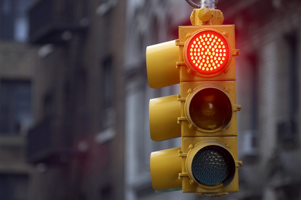 photo of a yellow traffic signal hanging in a city with the red light lit