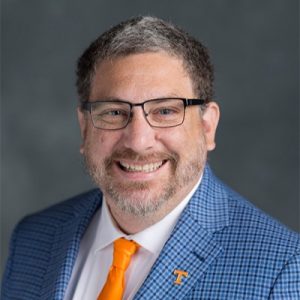 Kevin Heaslip professional headshot in blue suit and orange tie in front of grey background
