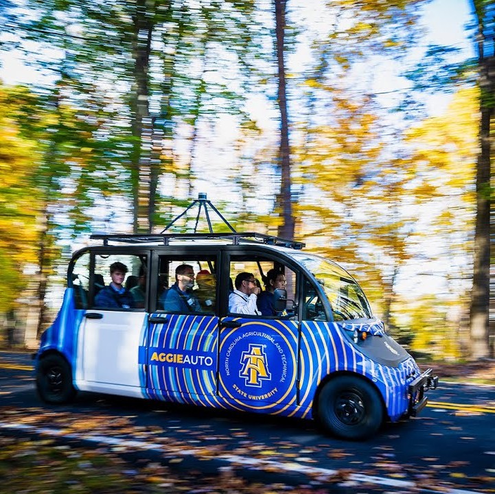 An Image of a project an affiliated university of CR2C2 worked on - a futuristic vehicle on a road in the fall that says "Aggie Auto" on the side.